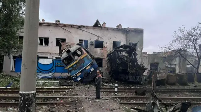 A railway employee stands next to a destroyed train at the compound of a depot after it was hit during an overnight Russian drone strike, amid Russia's attack on Ukraine, in Odesa