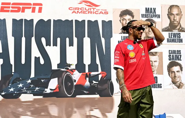 Lewis Hamilton stands in front of an Austin sign in the paddock