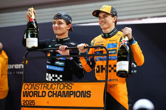Lando Norris and Oscar Piastri hold up champagne after McLaren won the constructors' championship