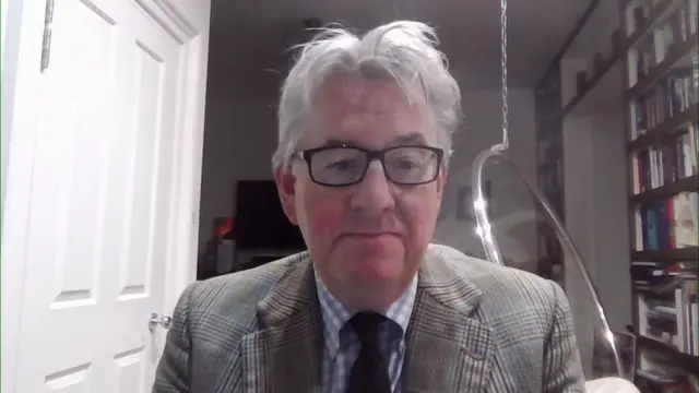 Robert Hardman, wearing a suit and tie, looks into the camera from his home office.