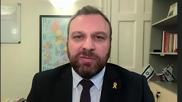 A man in a dark suit looks at the camera from inside the Israeli embassy in London.