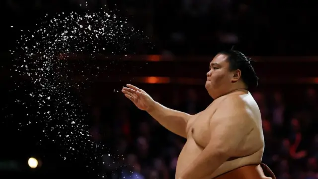 A sumo wrestler throws salt before a bout, which is pictured flying in the air