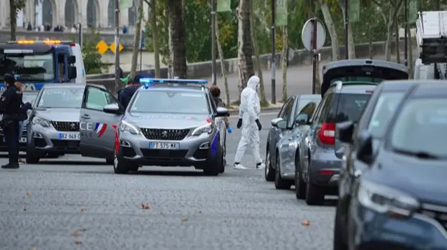 Police car in paris with its door open as an officer in a white hazmat suit patrols the area