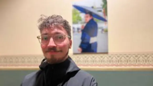 Cezar De Almeida Johansson smiling at the Royal Albert Hall, in front of a photo of a sumo wrestler