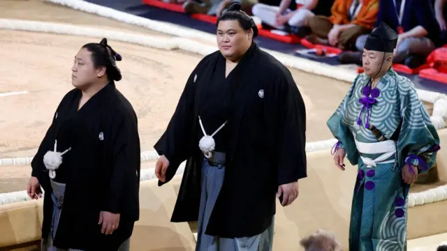 Onosato and Hoshoryu walk alongside the ring, with a referee following behind