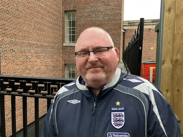 A man wearing an England football tracksuit top wearing glasses