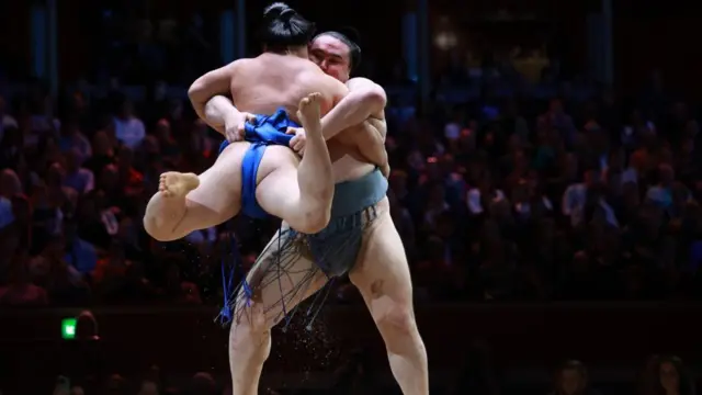 One sumo wrestler lifts another up during a bout