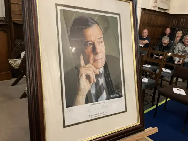 A portrait of Dickie Bird with mourners in the background