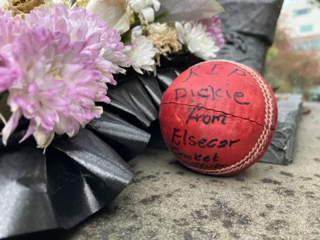 A signed cricket ball surrounded by floral tributes.