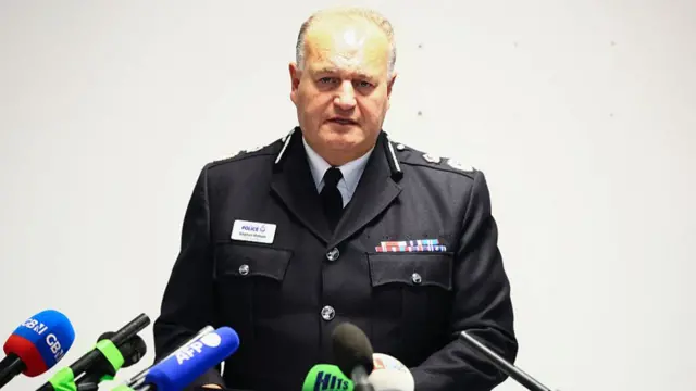 Greater Manchester Police Chief Constable Sir Stephen Watson speaking behind microphones at a podium.
