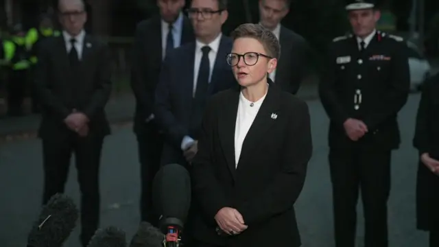 Bev Craig speaking to the media. Andy Burnham and a line of police officers stand behind her.