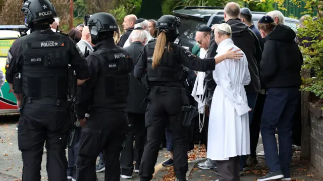 Police tend to a group of people near a synagogue in Manchester