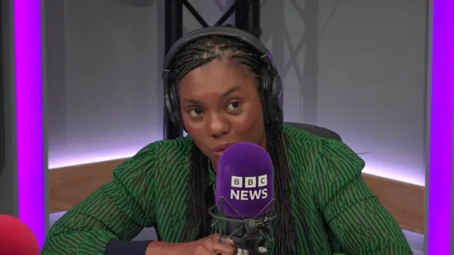 Kemi Badenoch pictured wearing a green dress in a BBC studio with a purple microphone in front of her.