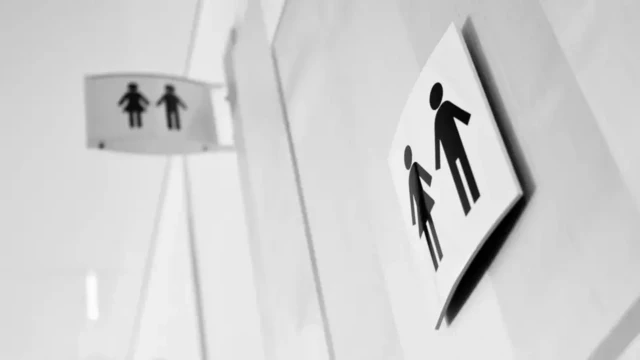 A female and male symbols on a gender neutral toilet sign on a white door.