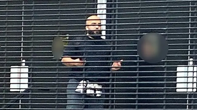 A man in a dark T-shirt behind a fence