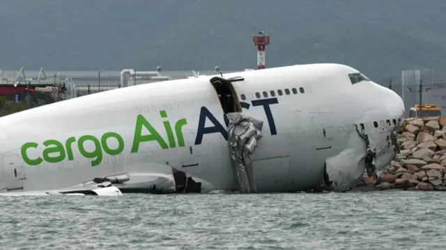 A damaged plane fuselage partially submerged in seawater.
