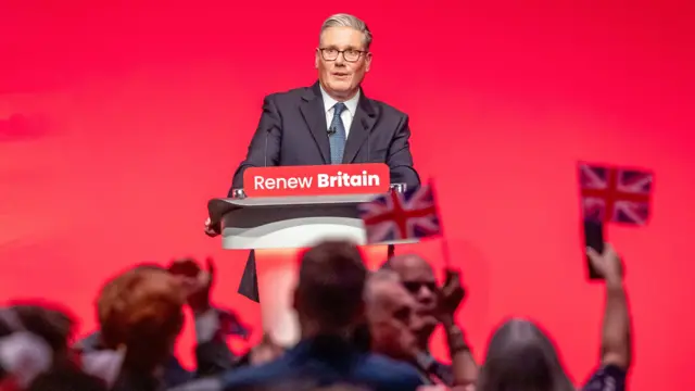 Starmer speaks into a microphone in front of a red backdrop