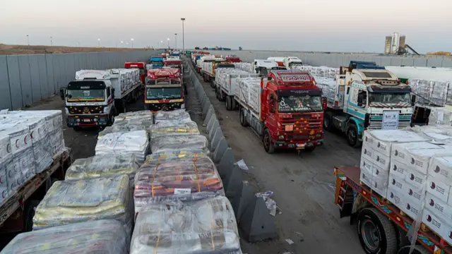 Trucks wait in a long line carrying aid pallets at Rafah crossing