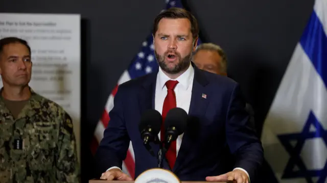JD Vance in a blue suit and red tie stands at a podium