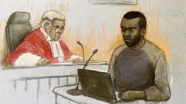 A drawing of a man with short dark hair and a grey/green top looking at a laptop at a desk with a man with white hair and a red gown in the background