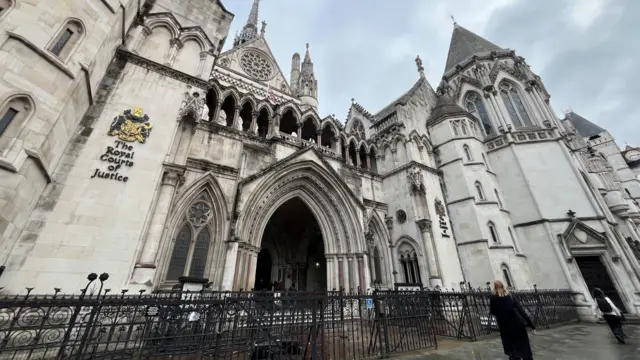 The front of the Royal Courts of Justice in London. A white stone building with ornate arches and turrets, and iron railings in front of it.