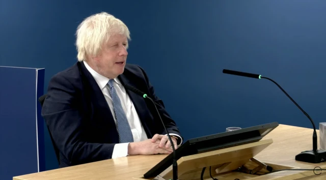 Boris deliberates whilst speaking at the Inquiry. He is sat at a desk.