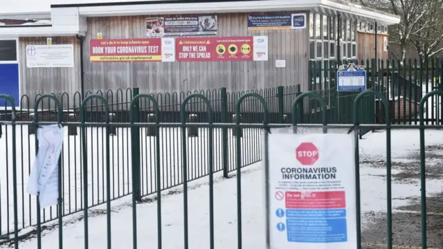 A school in the snow has lots of signs visible, telling people to book Covid tests and providing information on the pandemic.