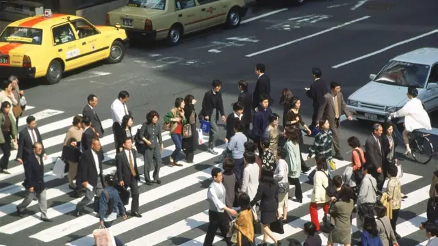 A photo from 1999 showing pedestrians crossing a busy road in Japan, with a row of yellow taxis in the background