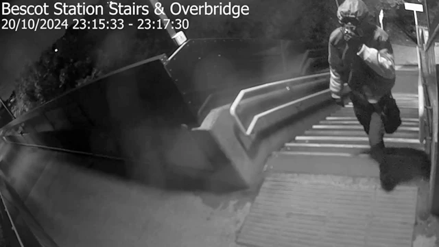 A black and white CCTV image of a man waliking up steps near a station
