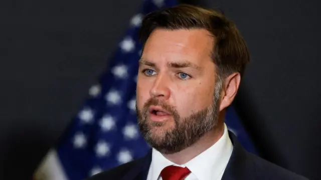 A close up of JD Vance in a black suit and red tie