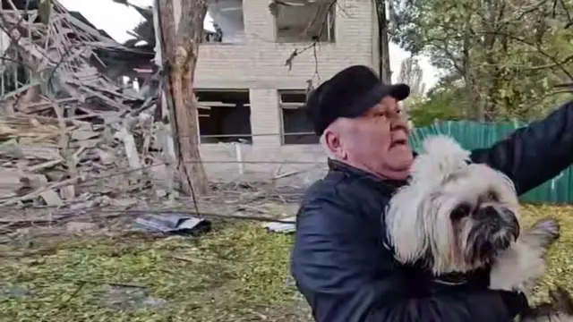 A man holds a dog at the same place as in the picture above