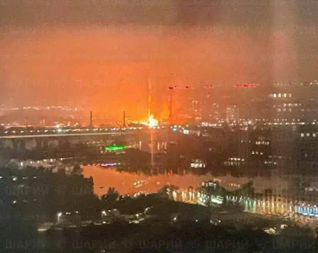 An image of a power plant on fire taken from across a river