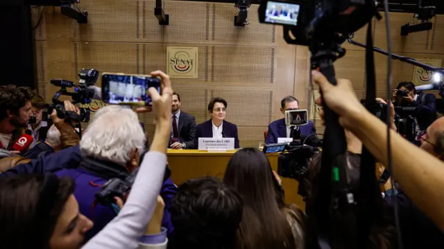 A cluster of journalists and cameras points towards the president and director of the Louvre, Laurence des Cars