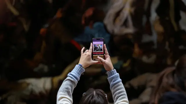 A visitor takes a picture with her mobile phone of the painting "La Liberte guidant le peuple" in the Louvre