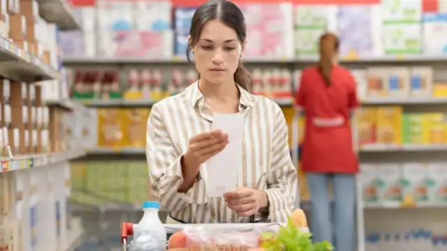 A woman inspects the bill of her groceries in an aisle.