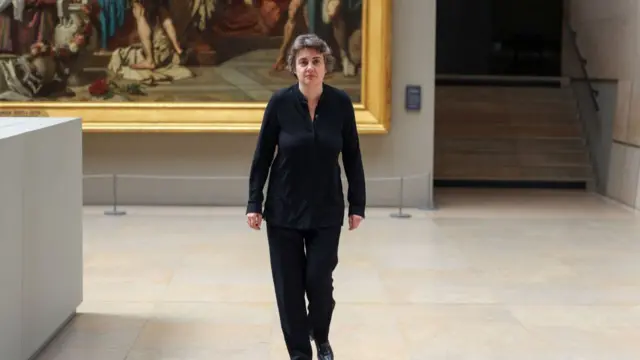 Laurence des Cars walking through gallery in the Louvre, hung with paintings