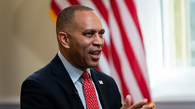 Hakeem Jeffries in a suit during a television interview in front of a US flag