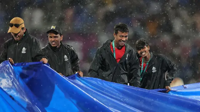 Ground staff bring on the covers as rain interrupts play during the ICC Women's Cricket World Cup India 2025