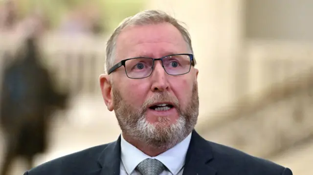 Doug Beattie, a man with grey hair and a brown and grey beard. He is wearing a dark grey suit, grey tie and white shirt. He is also wearing glasses.