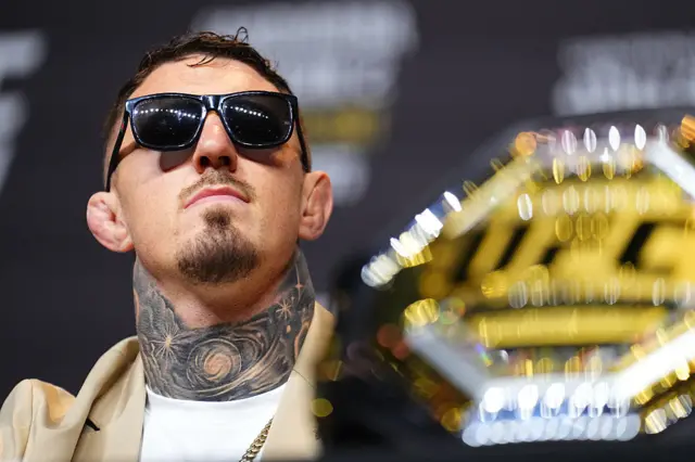 Tom Aspinall wearing sunglasses is next to the UFC heavyweight title