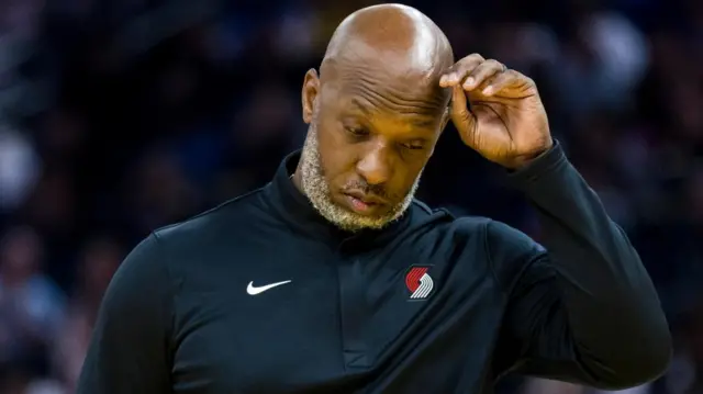 Portland Trail Blazers Head Coach Chauncey touches his bowed head while wearing a dark navy long-sleeved athletic top