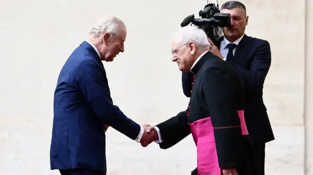 The King is met by Monsignor Leonardo Sapienza. They shake hands.