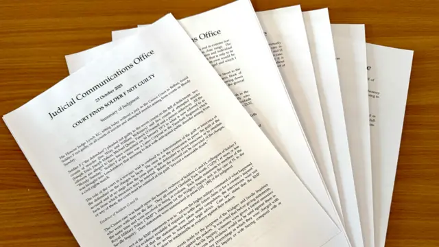 Several pages, the top one of which reads: 'Judicial Communications Office - 23 October 2025 - COURT FINDS SOLFIER F NOT GUILTY'