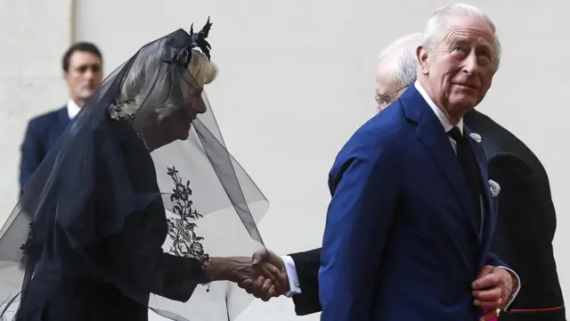 King and Queen arrive - Queen in black veil and flowered headdress, King in a blue suit looking upwards.