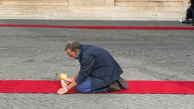 Man fixing red carpet onto a stone floor with a small hammer