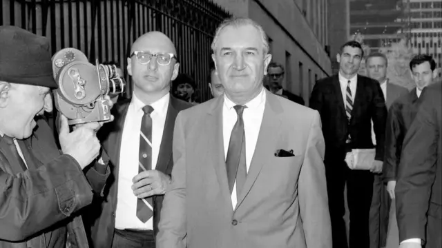 Bonanno wearing a suit and slight smirking as a photographer gets a close-up