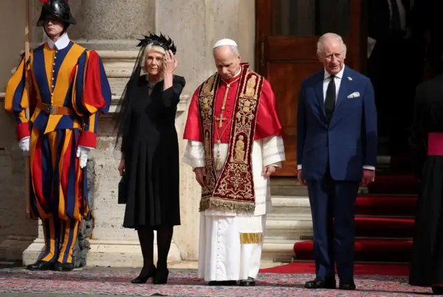 Left to right: Swiss Guard, Queen Camilla, Pope Leo, King Charles. All stand in the courtyard of San Damaso, Vatican
