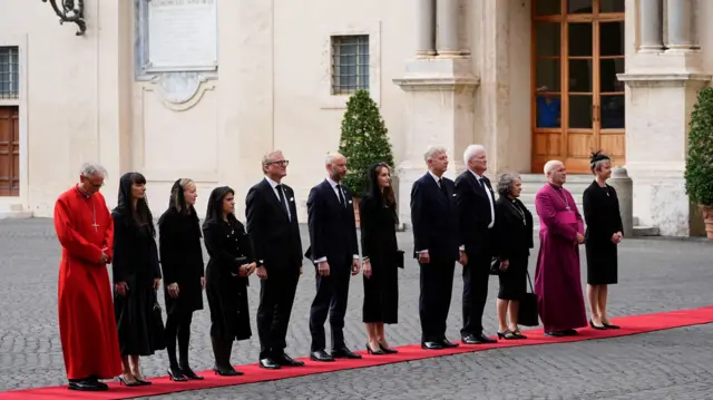 Yvette Cooper stands at the front of a line of people including members of the Royal Household staff along a red carpet as they await the arrival of the King and Queen