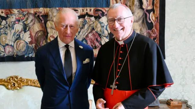 King Charles stands with Cardinal Pietro Parolin - both look towards the camera and smile