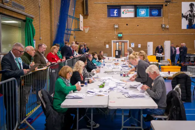 People counting the votes with party representatives stood behind a barrier